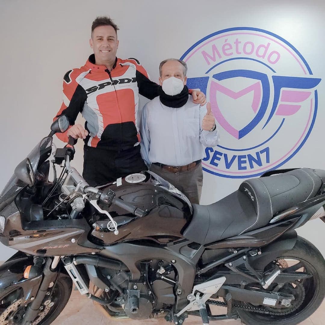 Un alumne de moto i el seu professor davant del logotip del Mètode Seven7.