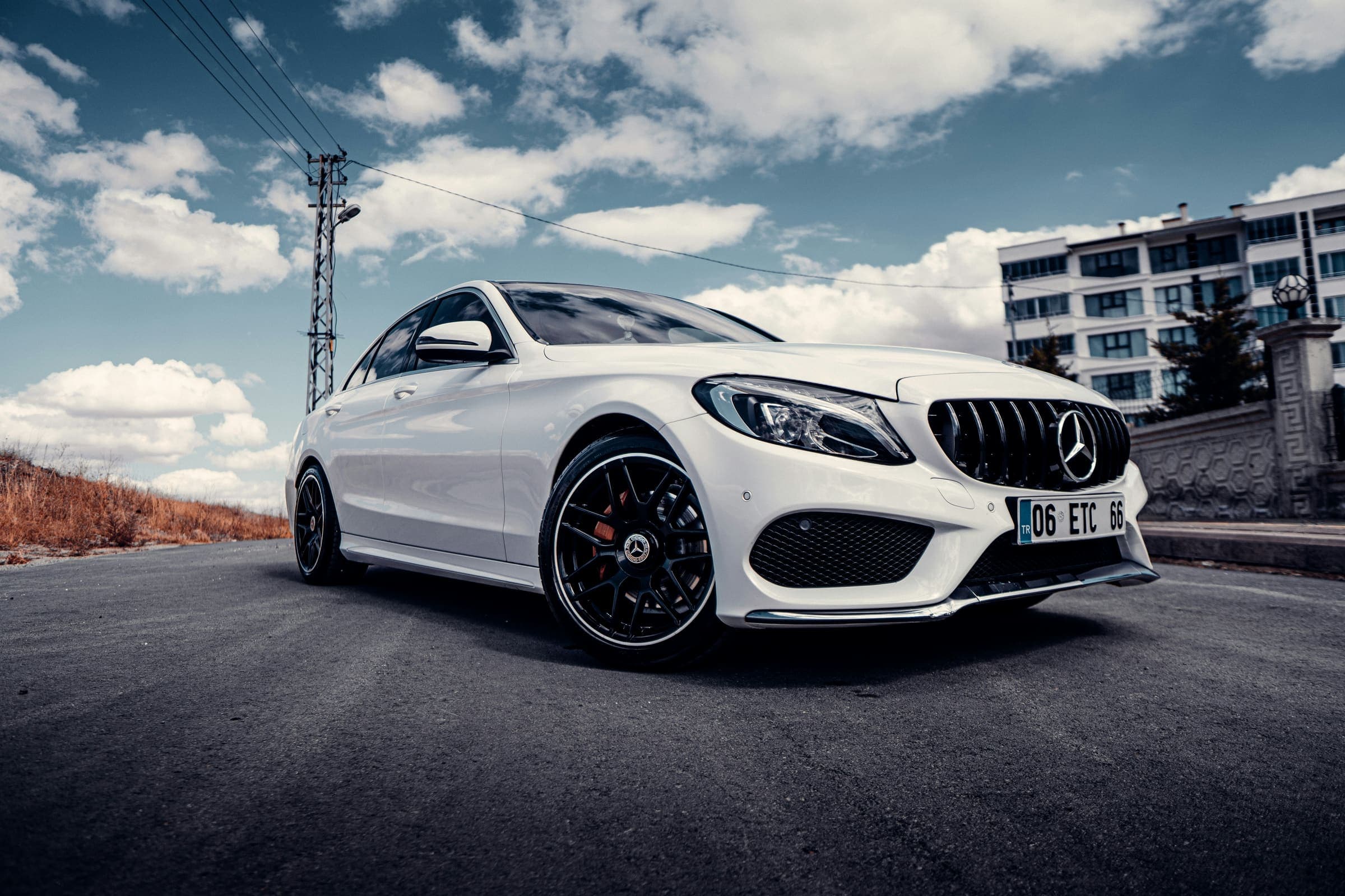 A white car parked on a road under a blue sky with clouds.